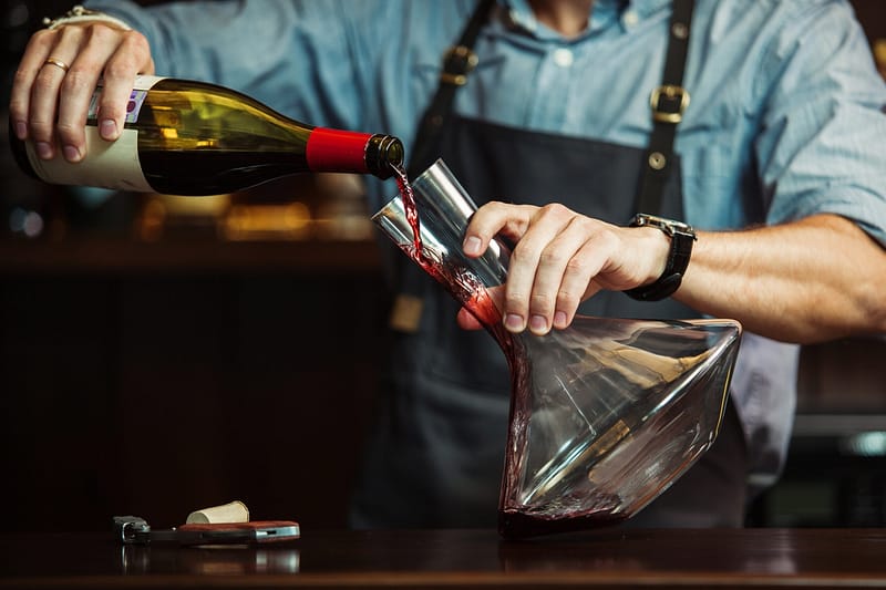 bouteille de vin rouge en train d'être versé dans un verre à décanter