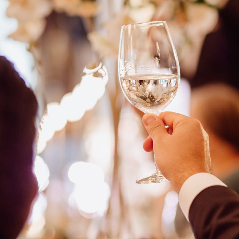 un marié habillé en costard pour son mariage regarde son verre de vin blanc